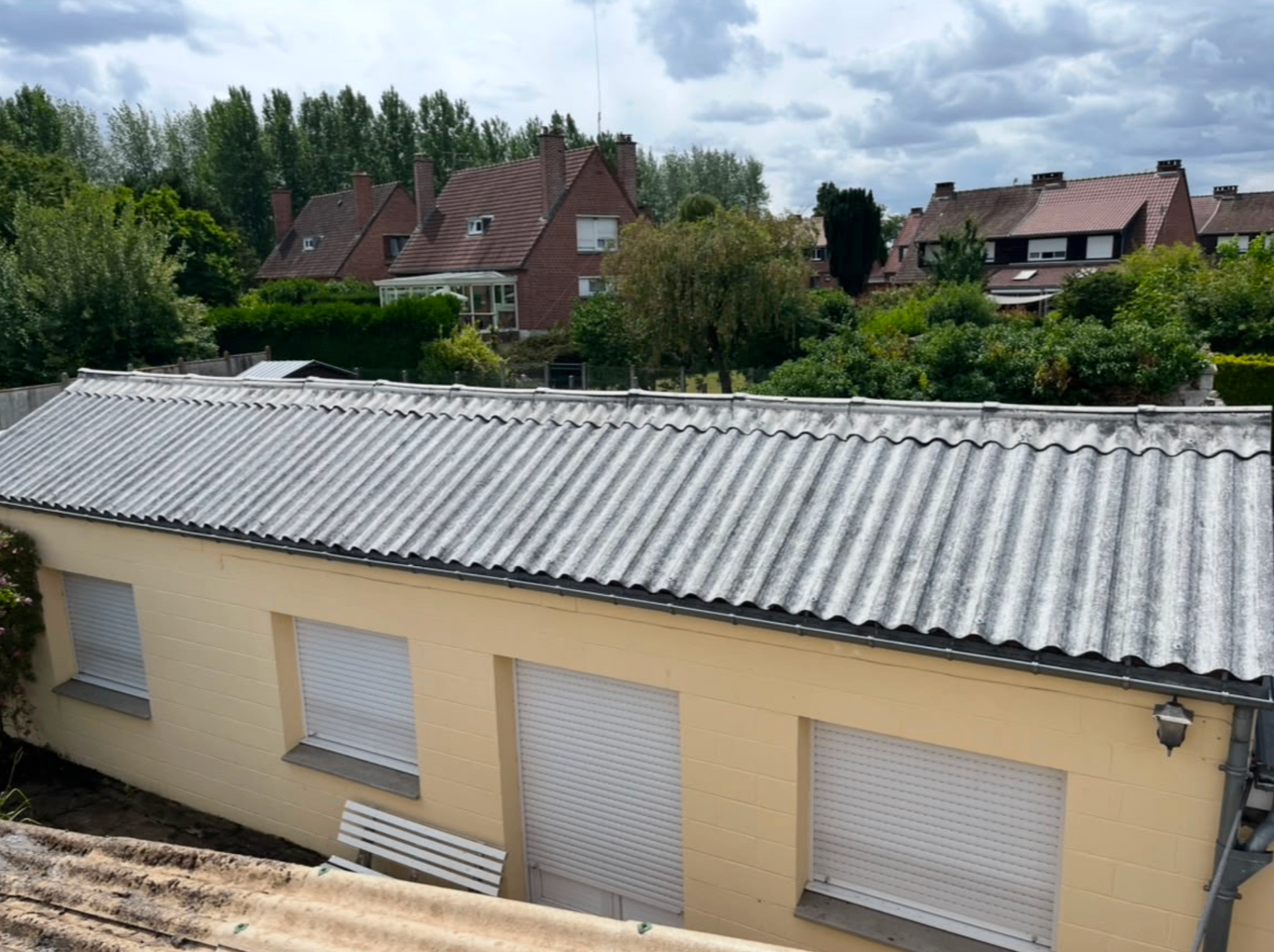 Toiture en bac acier gris ondulé sur maison claire avec volets